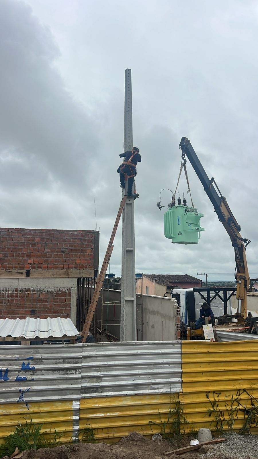 Trabalhador em altura próximo a transformador suspenso durante serviço de infraestrutura elétrica