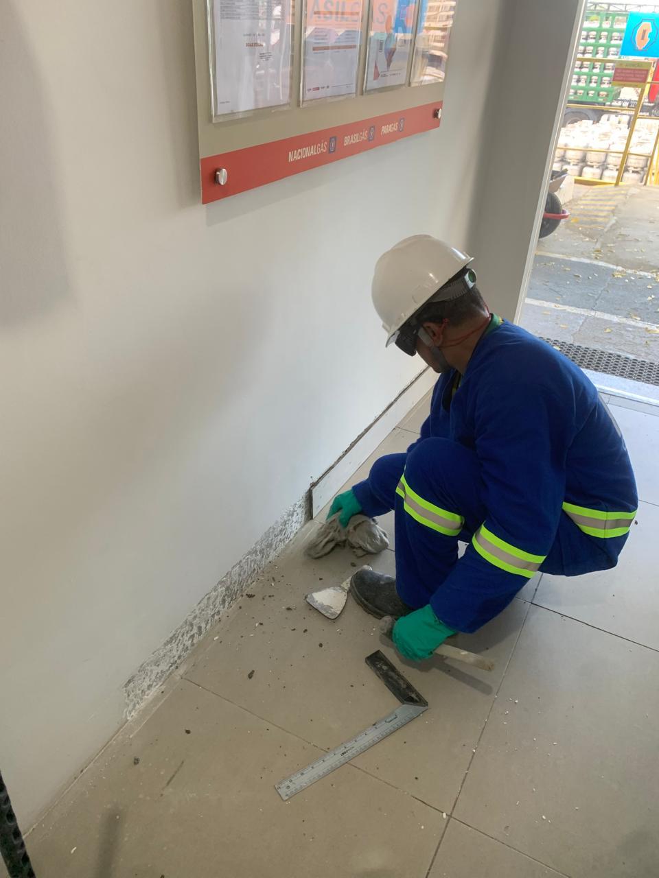 Profissional com uniforme e capacete faz reparo na parte inferior de uma parede